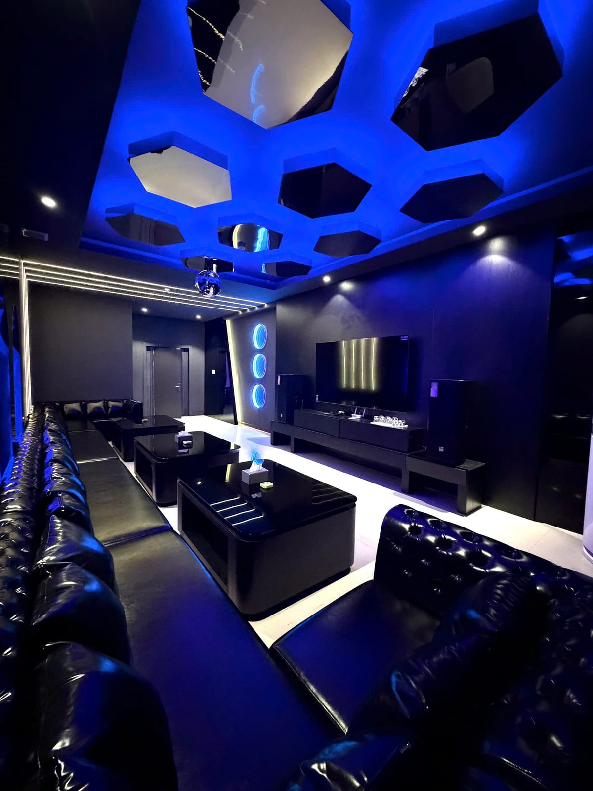 다낭 QQ LOUNGE 프라이빗 룸 — 블루 조명 육각 천장과 검은 가죽 소파, 대형 TV와 스피커