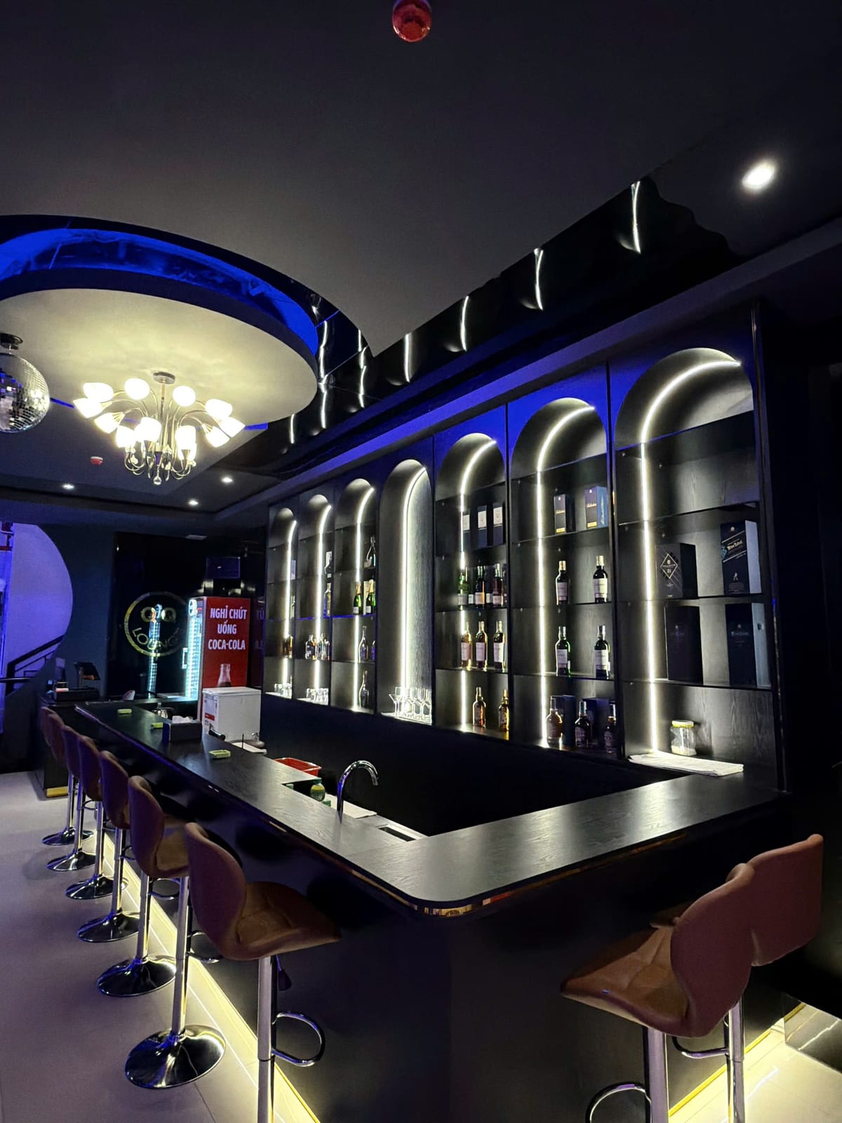 다낭 QQ LOUNGE 바 카운터 — 아치형 주류 진열장과 높은 스툴, 벽면 QQ LOUNGE 로고